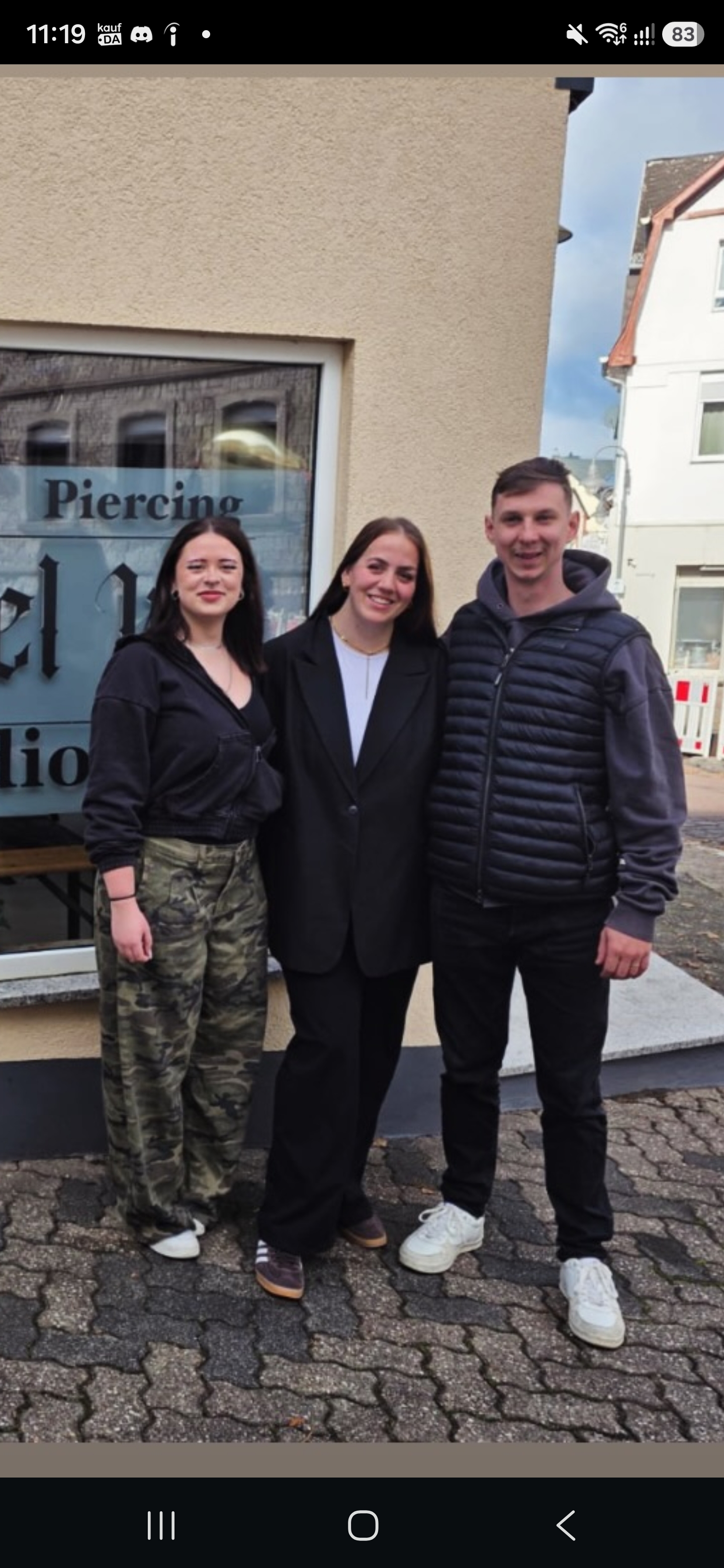 Jaana, Lana und Rommel von links nach rechts vor dem Studioschaufenster mit Piercing-Schriftzug